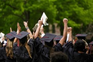 A group of graduates with their hats on putting their arms up in celebration, ready to find their first secretarial job.