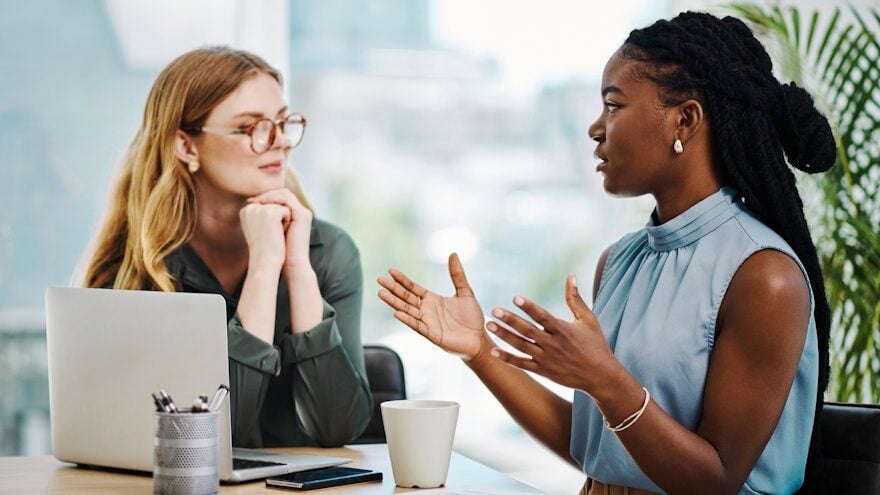 Two young professional women talking over a laptop