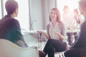 A woman sitting on the chair trying to improve her interview technique. She’s talking to two men, gesturing and smiling.
