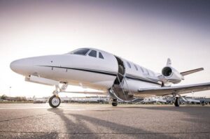 A small private plane on a tarmac with an open door. In the background, there’s a small airport.