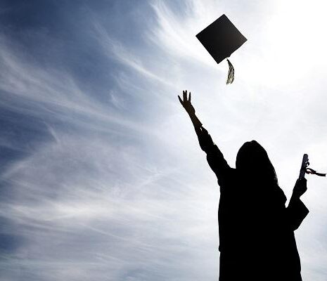 A black shadow of a graduate throwing their hat up into the air with a degree and sunny background.