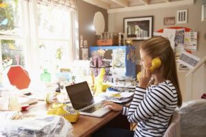 A woman in a flexible working arrangement using a yellow landline phone in a sunlit home office.