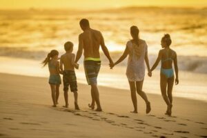 A family of five walking along a beach at sunset, with the parents taking all of their holiday entitlement.