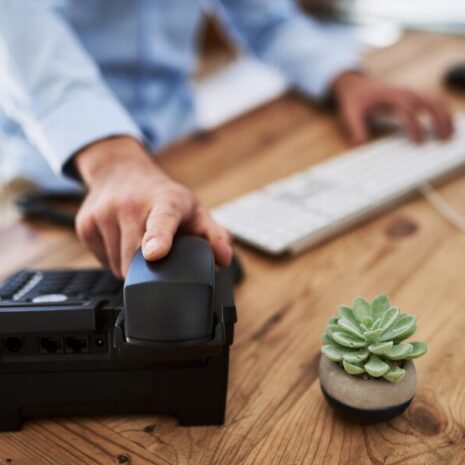 Cropped shot of a man holding the receiver of a telephone in a virtual office with a cactus on the desk.