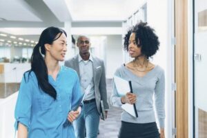 Two women walking down a hallway in a workplace with their male colleague walking behind them.