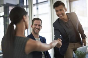 Three business people sit at a desk and shake hands, attracting the right candidates.