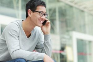 A man sitting outside a building and smiling while taking part in a phone interview.