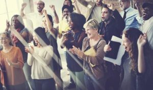A group of people cheering, clapping, laughing and smiling in an office.