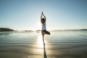 A private PA practicing yoga on a beach at sunset.