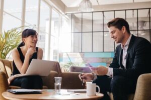 A private PA talks to a recruiter in a cool and modern open plan office while holding a laptop.