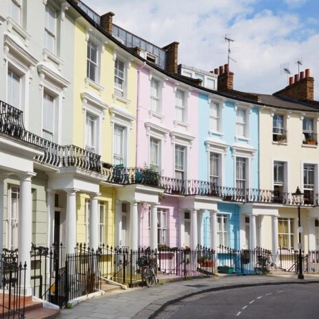 Colourful West End London houses in Primrose hill lined up. They are painted grey, yellow, pink, blue and beige.