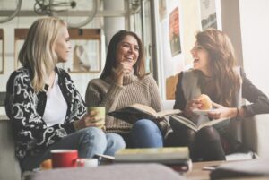 Three girls learning and eating in a cafe with books, coffees and snacks while sitting on a couch.