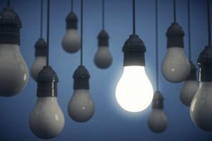 Eleven light bulbs with one turned on with a blue background.