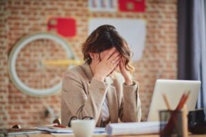 A private PA at work with her hands on her face, stressed while using her laptop computer.