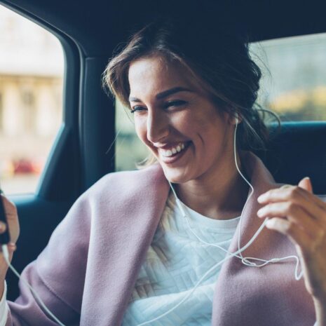 Young woman with smart phone and headphones on the back seat of a car.
