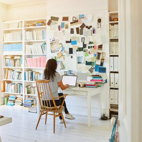 Rear view of pregnant woman sitting in home office and working on laptop