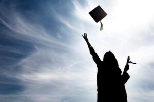 A shadow of a graduate in a cap and gown, throwing her hat into the air on a sunny day.
