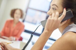 A career receptionist picking up the phone at her office with her colleague in the background.
