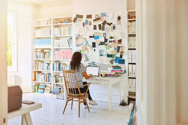 A woman in a remote working role in her home office with a bookshelf full of books and a laptop computer.