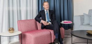 William Hanson, Etiquette Expert, sitting on a pink sofa with his legs crossed and arms folded in a classy manner.