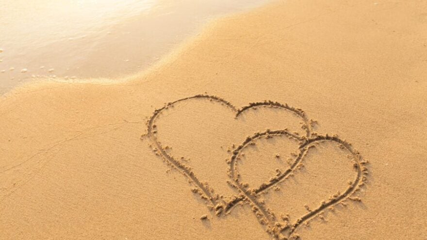 Two hearts drawn out of the sand on Love Island, representing the reality TV show.