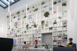 A man sitting in an open-planned, community space with a large wall with plants, frames and artwork.
