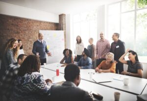 A group of colleagues in a business meeting, most laughing and smiling while discussing company matters.
