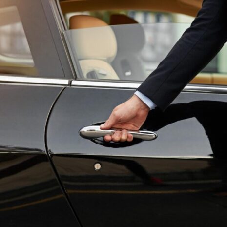 A chauffeur in a suit, ready to open the car door for his principal.