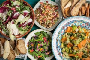 Various plates of catered lunch sitting on a tablecloth, with salads, bread and other delicious dishes.