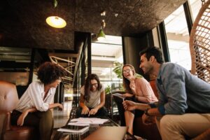A group of four young creative professionals in a meeting in a modern, well-lit office. They are talking and laughing.