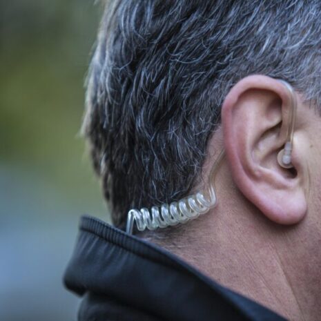 A close up on a close protection officer’s earpiece while he’s working a job outside, protecting the principal who hired him.