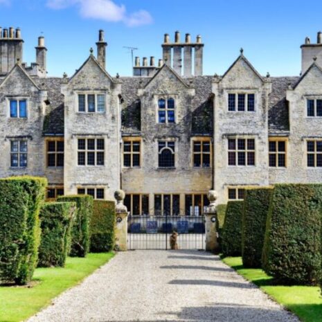 A large mansion and country estate where a house manager works. It is sunny and there is a beautiful driveway and hedges.