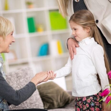 Little girl has an introduction to her new nanny in her bedroom while her mother stands behind her with pink flowers.
