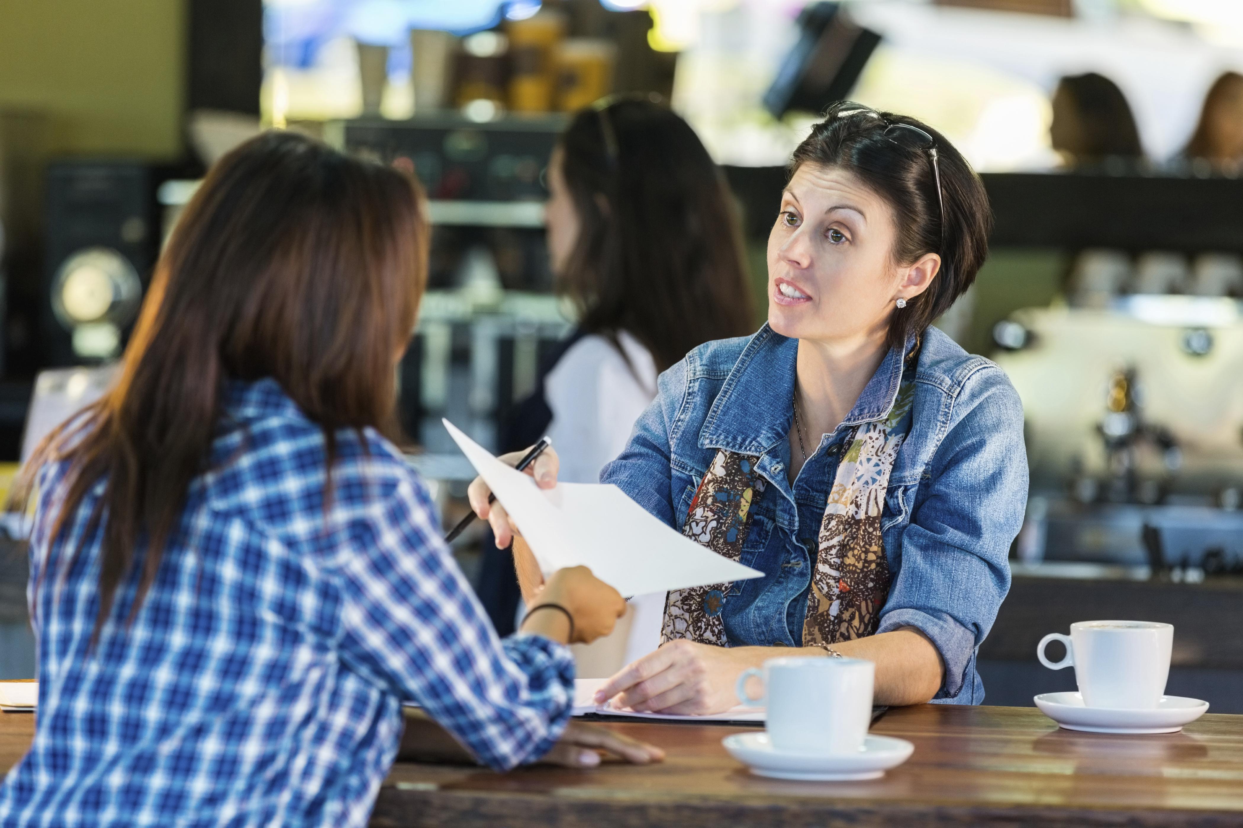 two women sitting at a cafe talking and referring to papers