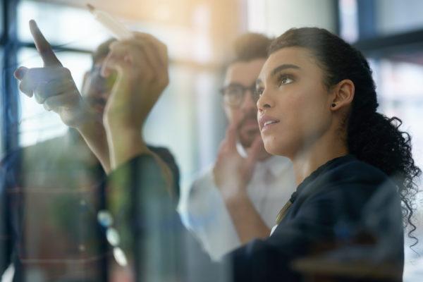 Shot of a group of colleagues brainstorming together on a glass wall in an office