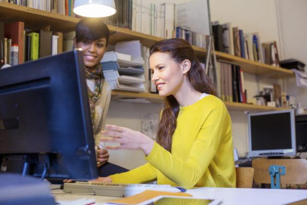 Image of two young women working together on a computer in their startup office