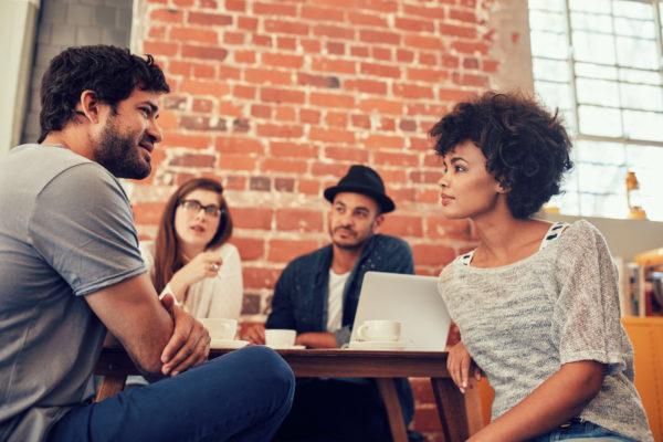 Portrait of young friends sitting at a cafe table and talking. Group of young people meeting at a coffee shop.