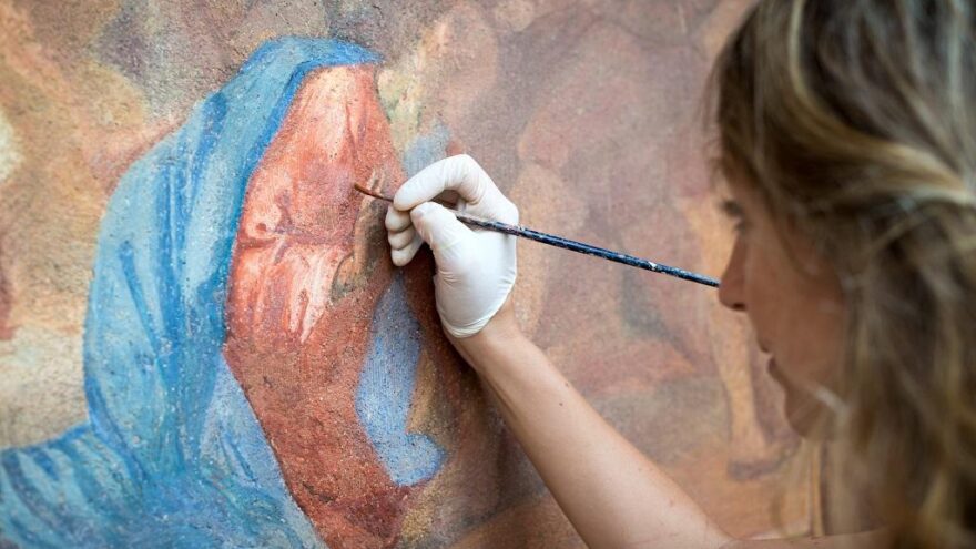Restorer working on antique outdoor chapel fresco in Italy: Painting restoring of religious art