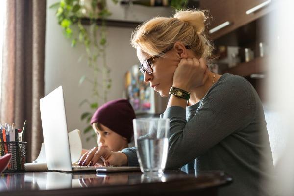 Woman on a laptop with a toddler next to her at home