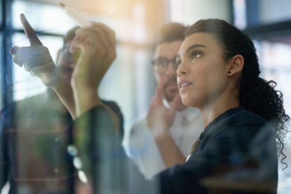 Shot of a group of colleagues brainstorming together on a glass wall in an office