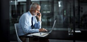Shot of a mature businessman using his laptop and phone at work