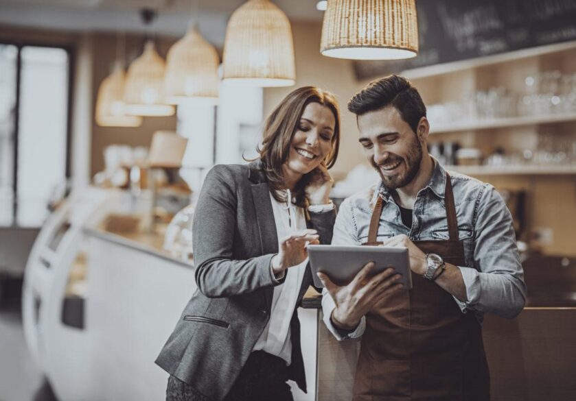 cafe owner and employee barista standing inside a coffee shop looking at new menu on a digital tablet