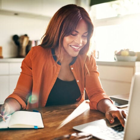 Woman sitting at the table working on her laptop smiling