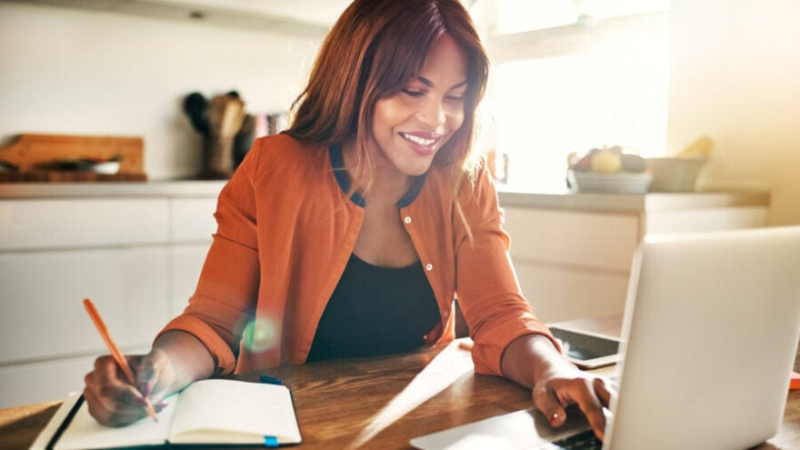 A female human resources professional sitting at her dining room table to work from home, smiling and chatting to her team.