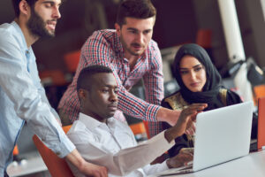 A group of four human resources staff working and talking in an office connected with tech devices like tablets and laptops.