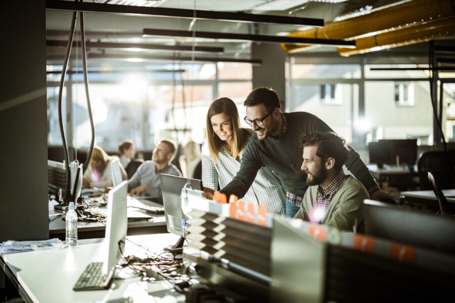 A group of IT colleagues working together around a computer in a busy office.