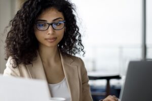 A young businesswoman working on a laptop while reading notes.
