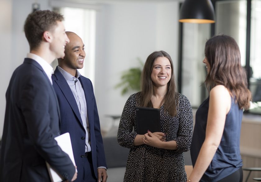 A group of colleagues smiling and talking in an office.