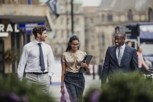 Three smartly dressed business people smiling and talking on city street.