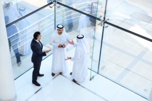Three middle eastern business people having a conversation in a modern glass office.